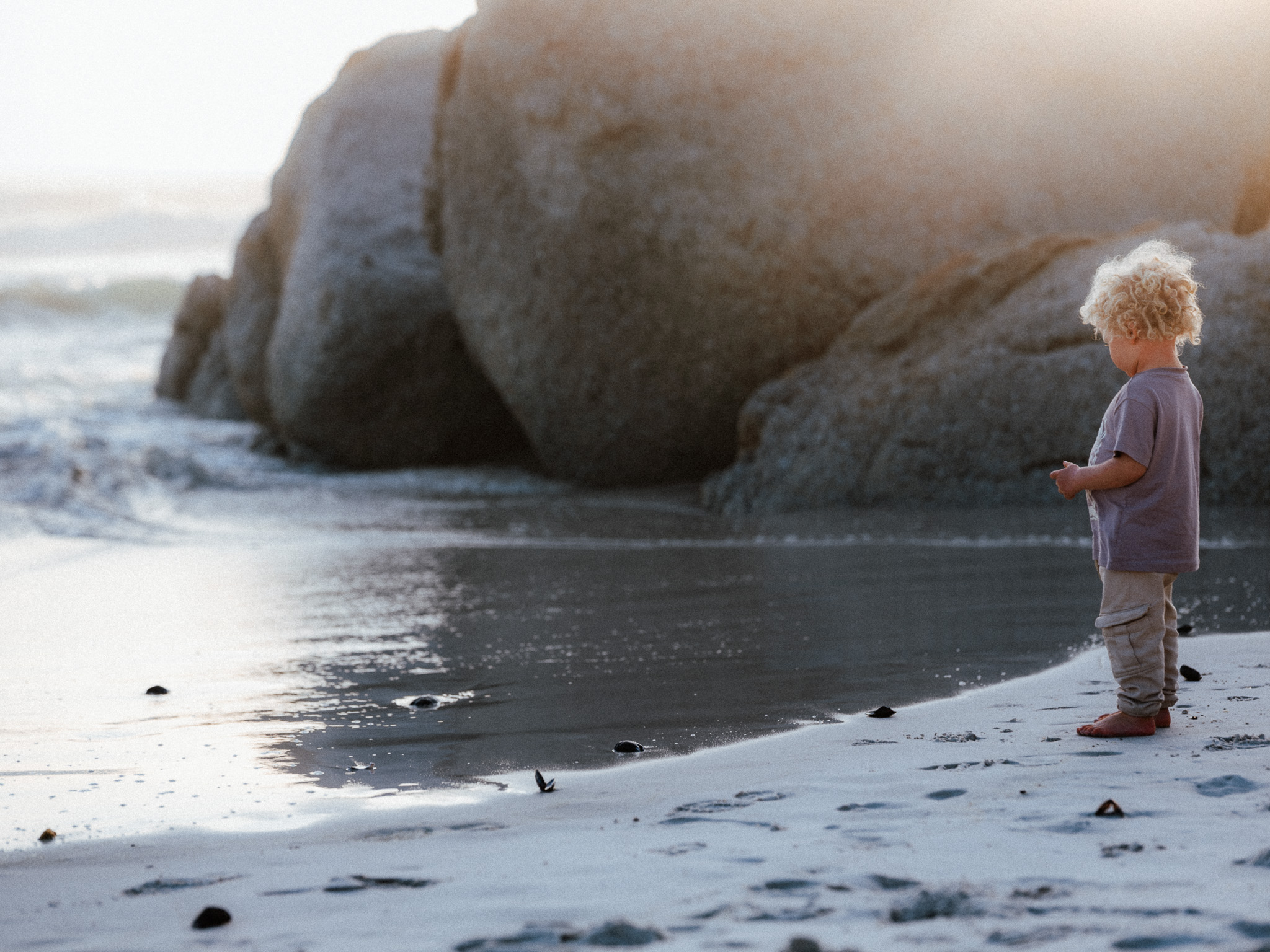 A child standing at the shoreline at dusk, beside a dark rock
