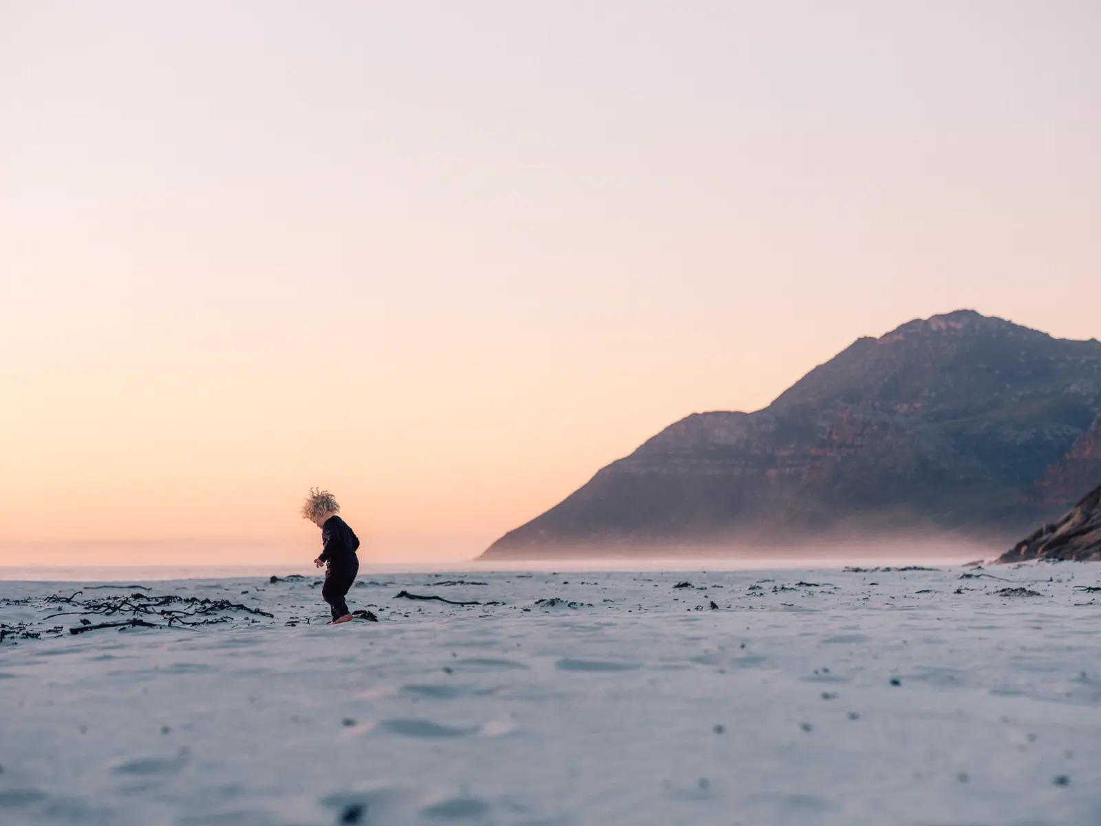 A child on the sand at dusk, a mountain behind