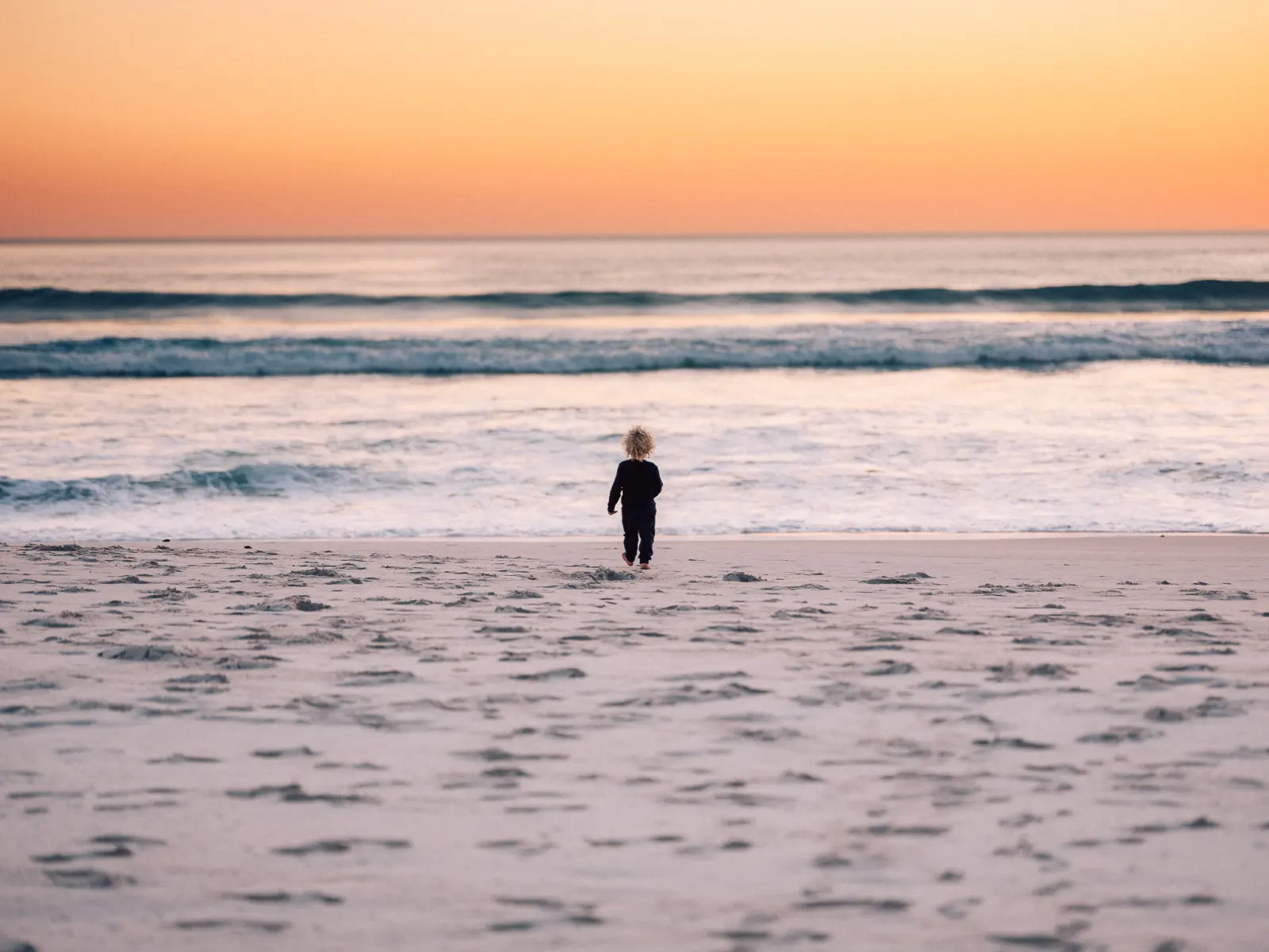 A child on the beach under a sunset sky