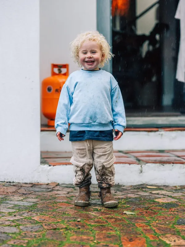 A child in a blue sweater, laughing in the doorway